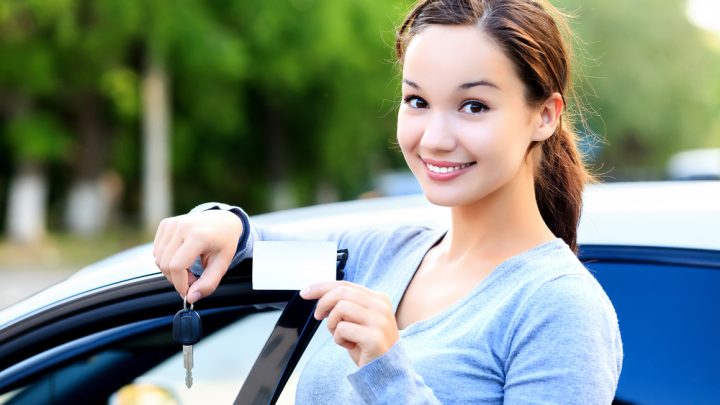 Young woman driver smiling with car licence and key