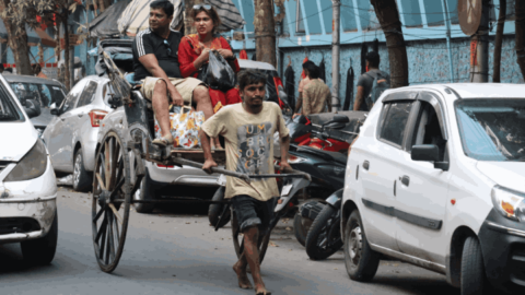 A bare foot rickshaw wallah pulls a disgruntled-looking couple along
