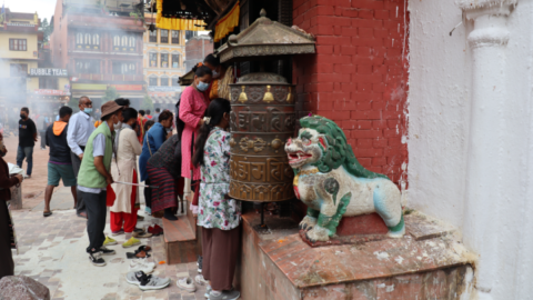 The entrance to a small temple that adorns the side of the stupa, with a snow lion statue beside it