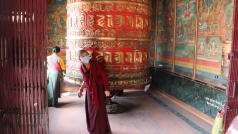 A nun circumnavigates a huge prayer wheel that must reach close to three metres high