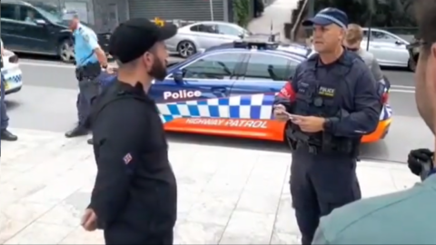 A NSW police officer issues National Socialist Network leader Thomas Sewell with a public safety order